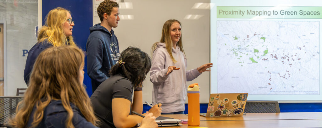 A student gives a presentation to her peers at a whiteboard.