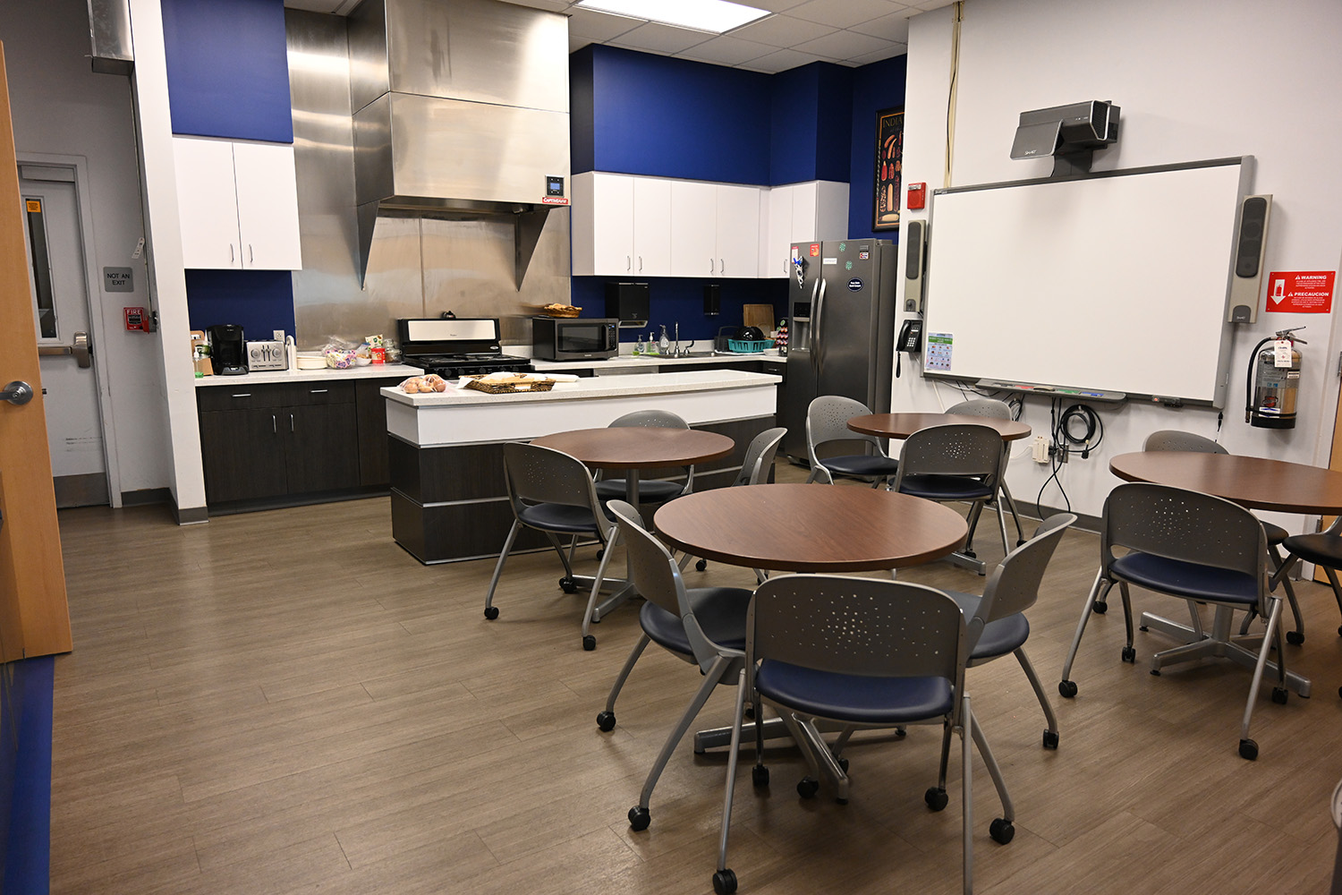 Round tables with chairs in a shared kitchen space in an office setting. There is a whiteboard near the tables.