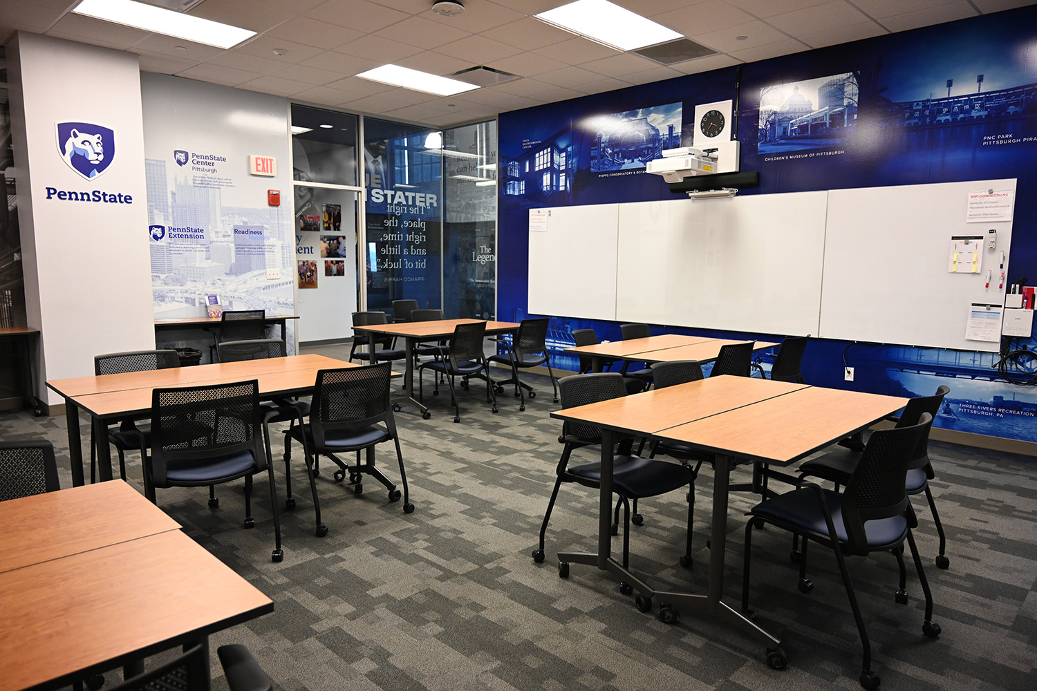 A classroom with a wide whiteboard at the front and several rectangular tables with chairs.