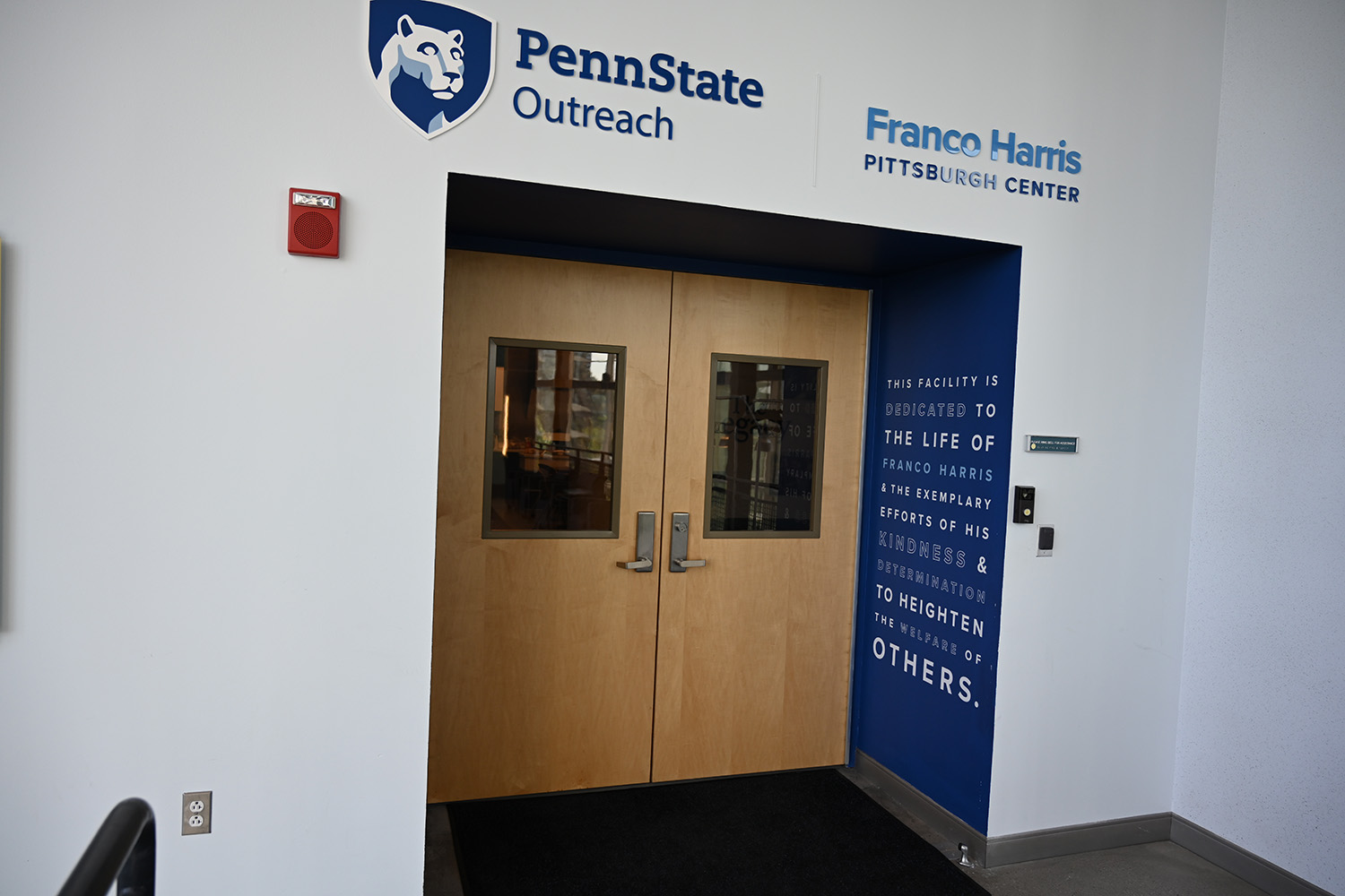 A doorway with Penn State Outreach and Franco Harris Pittsburgh Center written overhead and the quote, "This facility is dedicated to the life of Franco Harris and the exemplary efforts of his kindness and determination to heighten the welfare of others" written inside the doorway.