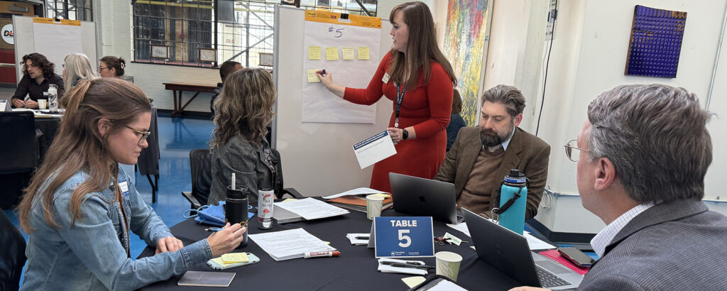 Professionals sit at a table and take notes.