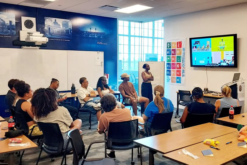 Student leaders participating in RA training sit in a classroom and watch a presentation on a tv.