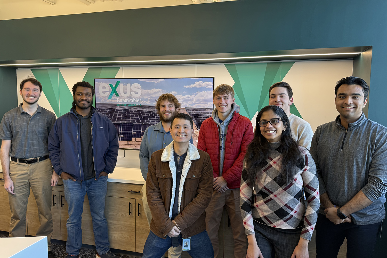 A group of students stands in front of the Exus Renewables sign.