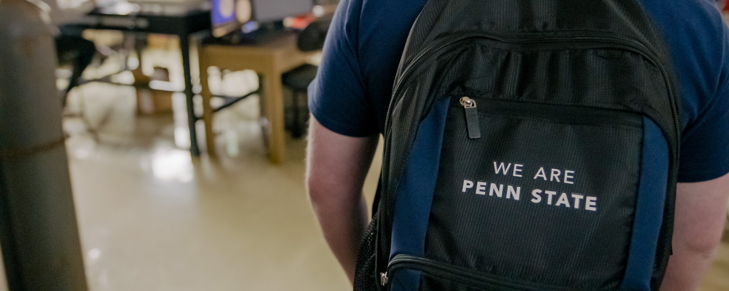 Student wearing a backpack with text 'We Are Penn State'