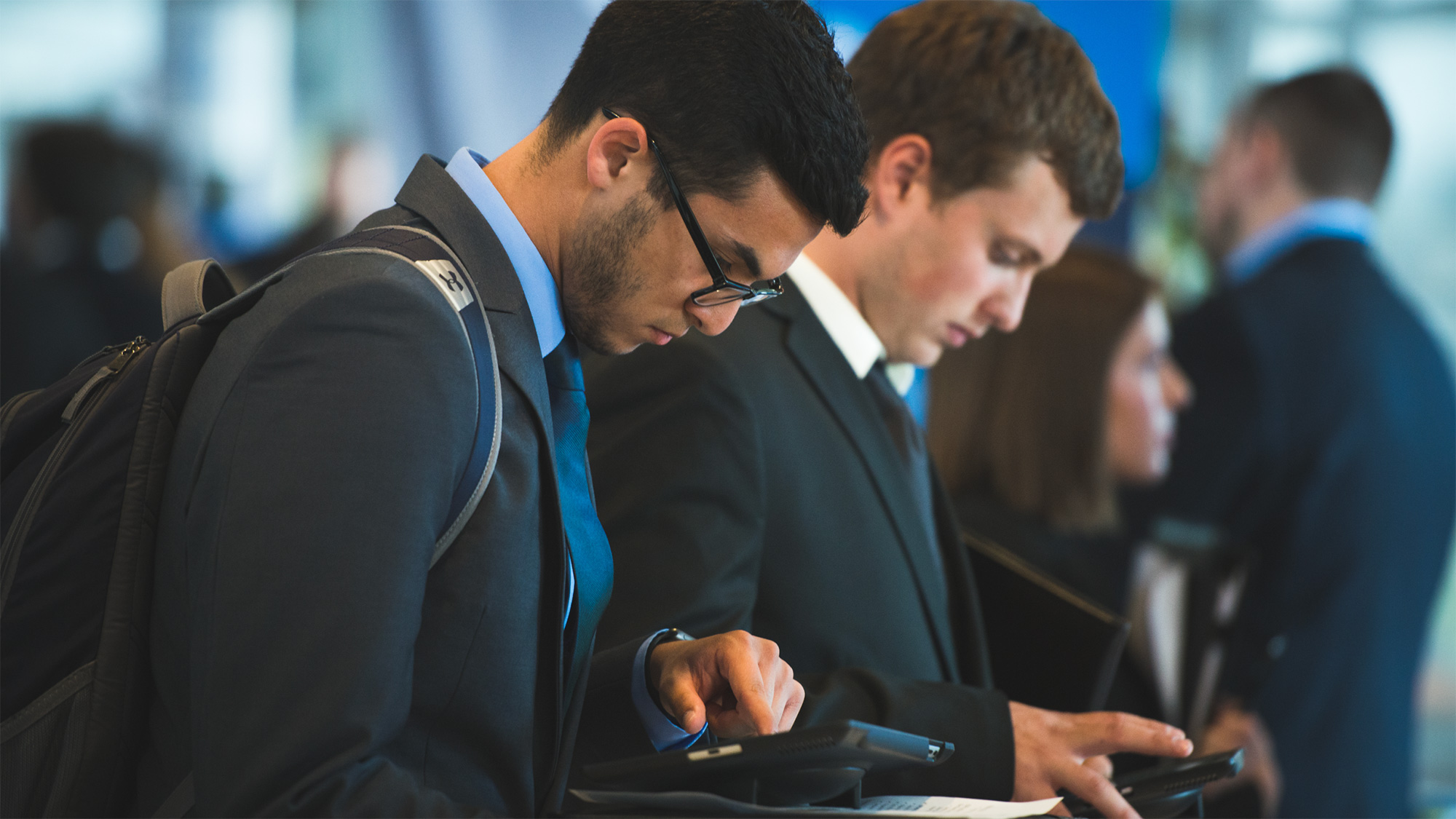 Two students, dressed in business suits, look at mobile devices